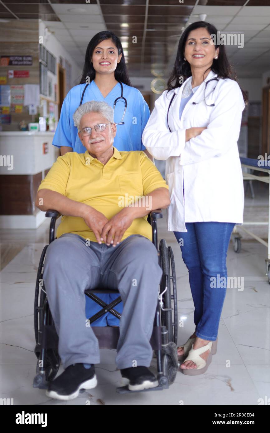 Indische Krankenschwester sieht sehr glücklich aus, grüßt einen älteren Patienten im Rollstuhl im Krankenhaus und lächelt - Healthcare-Konzepte. Stockfoto