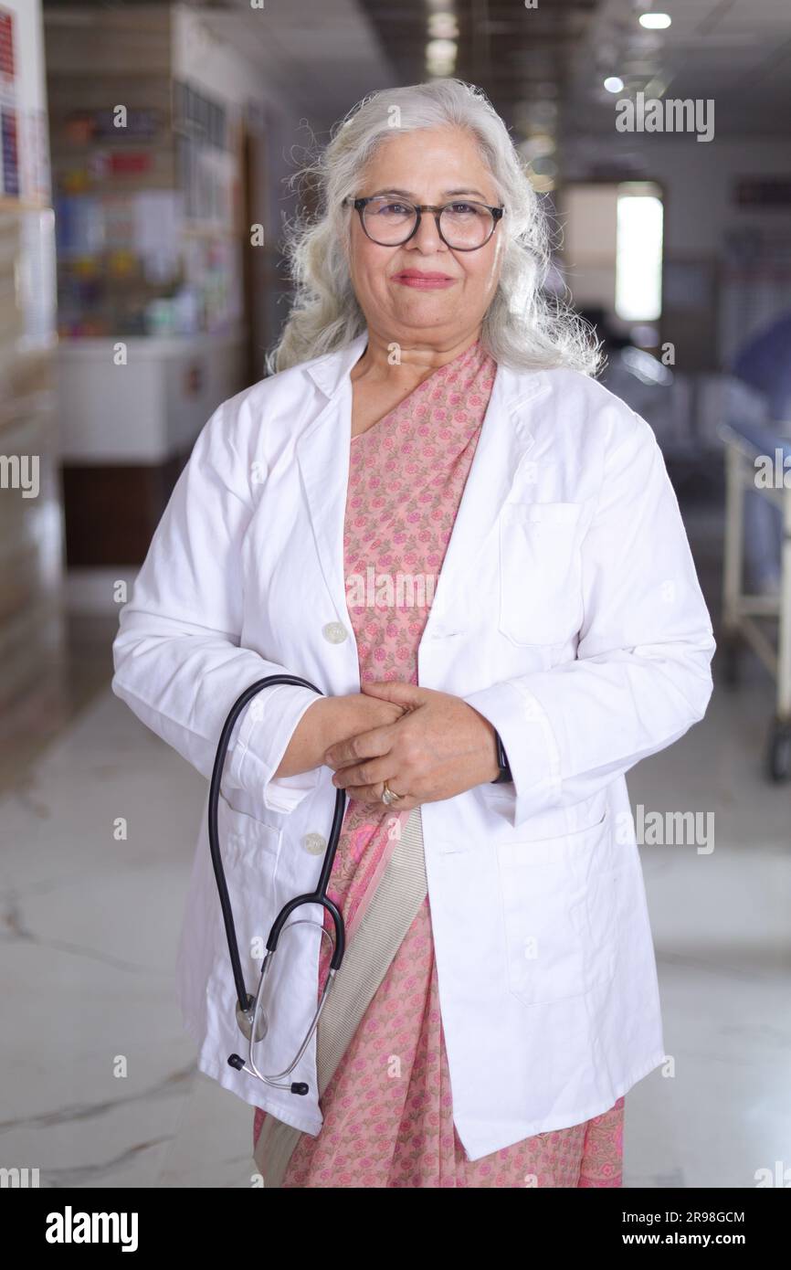 Porträt einer Oberärztin mit überkreuzten Armen im Krankenhauskorridor. Happy Indian Doctor White Laborkittel Stockfoto