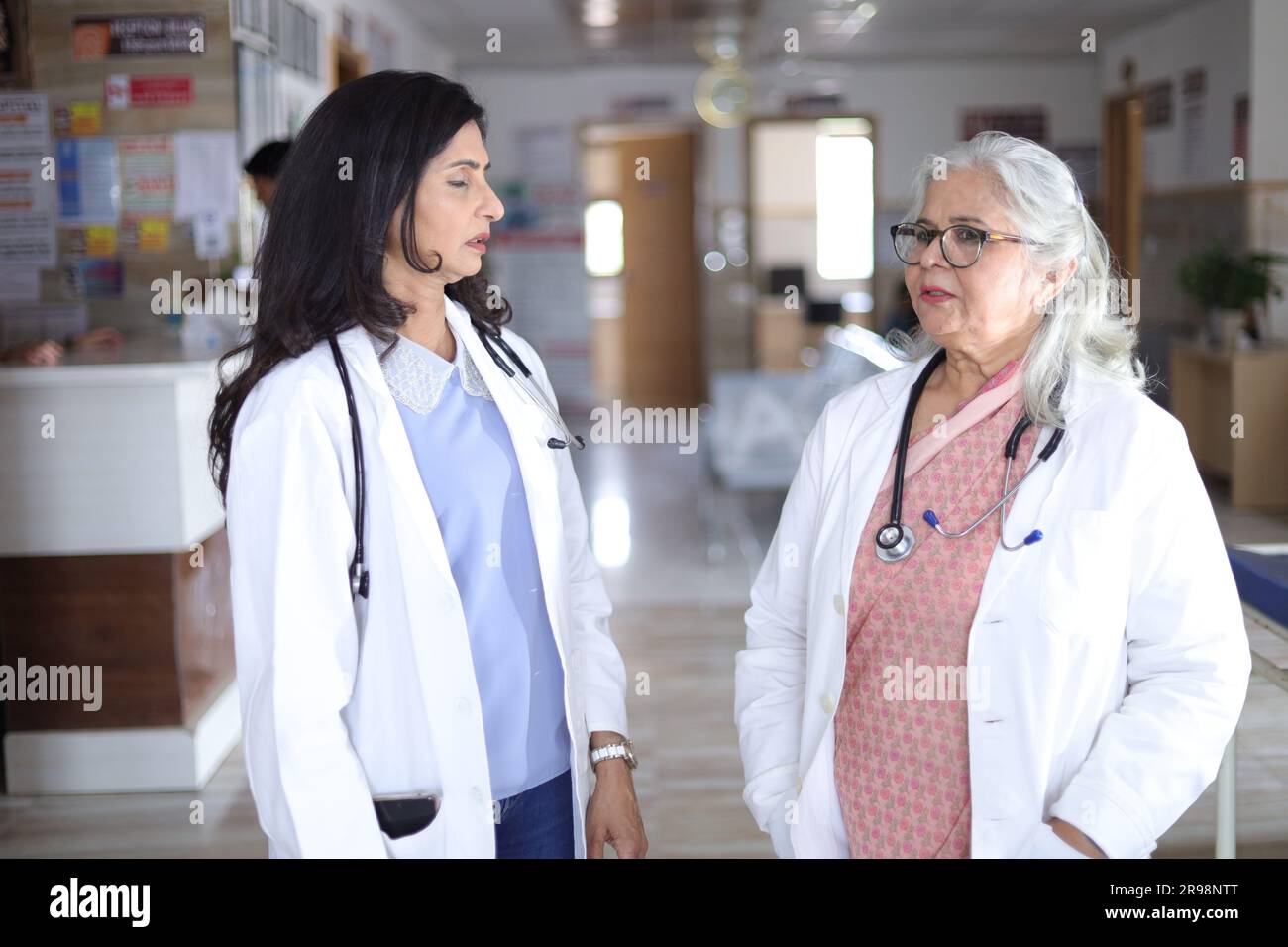 Ärzte lachen und reden auf dem Flur. Ältere Ärztin und junge Ärztin. Arzt liest Patientenbericht über Papiere oder medizinische Dokumente Stockfoto