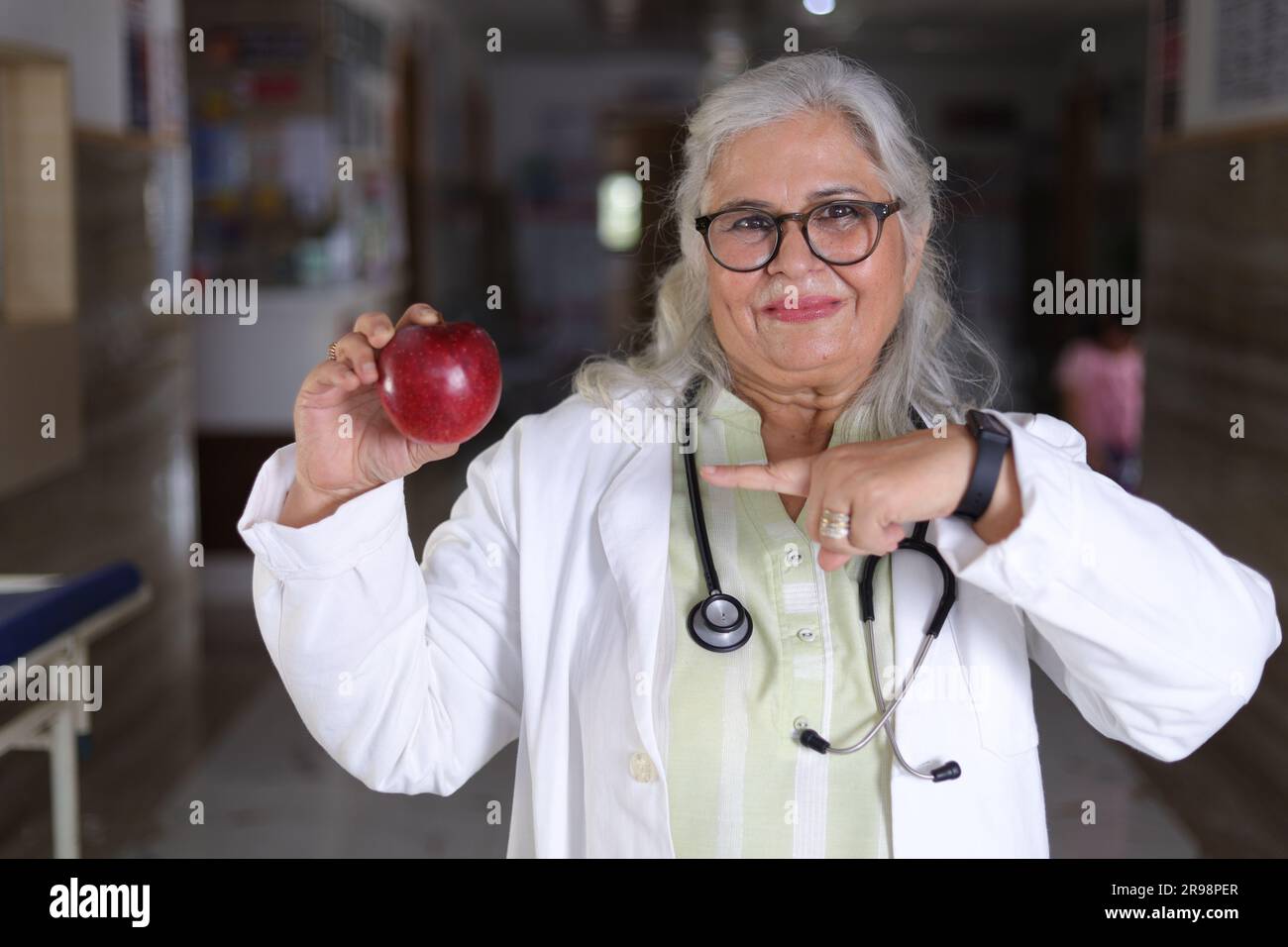 Die Botschaft zu zeigen, um eine bessere Gesundheit und einen sehr gesunden Ernährungsplan zu haben. Attraktive Ärztin mit einem lächelnden weißen Fell und einem Apfel. Stockfoto