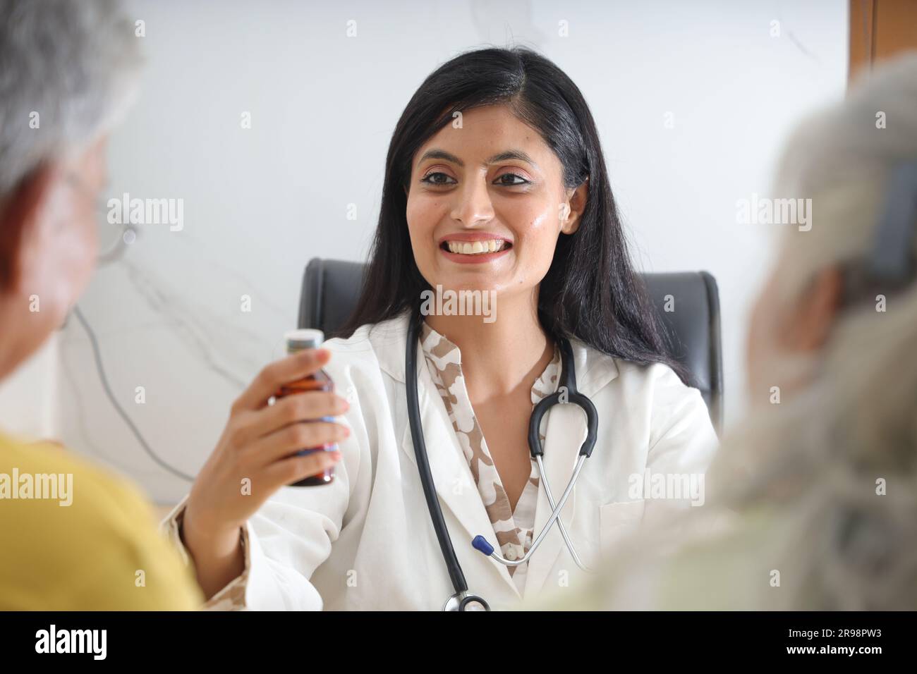 Attraktiver junger indischer Arzt, der mit einem Seniorenpatienten im Wohnzimmer eines Pflegeheims sitzt. Ein älterer Patient im Gespräch Stockfoto