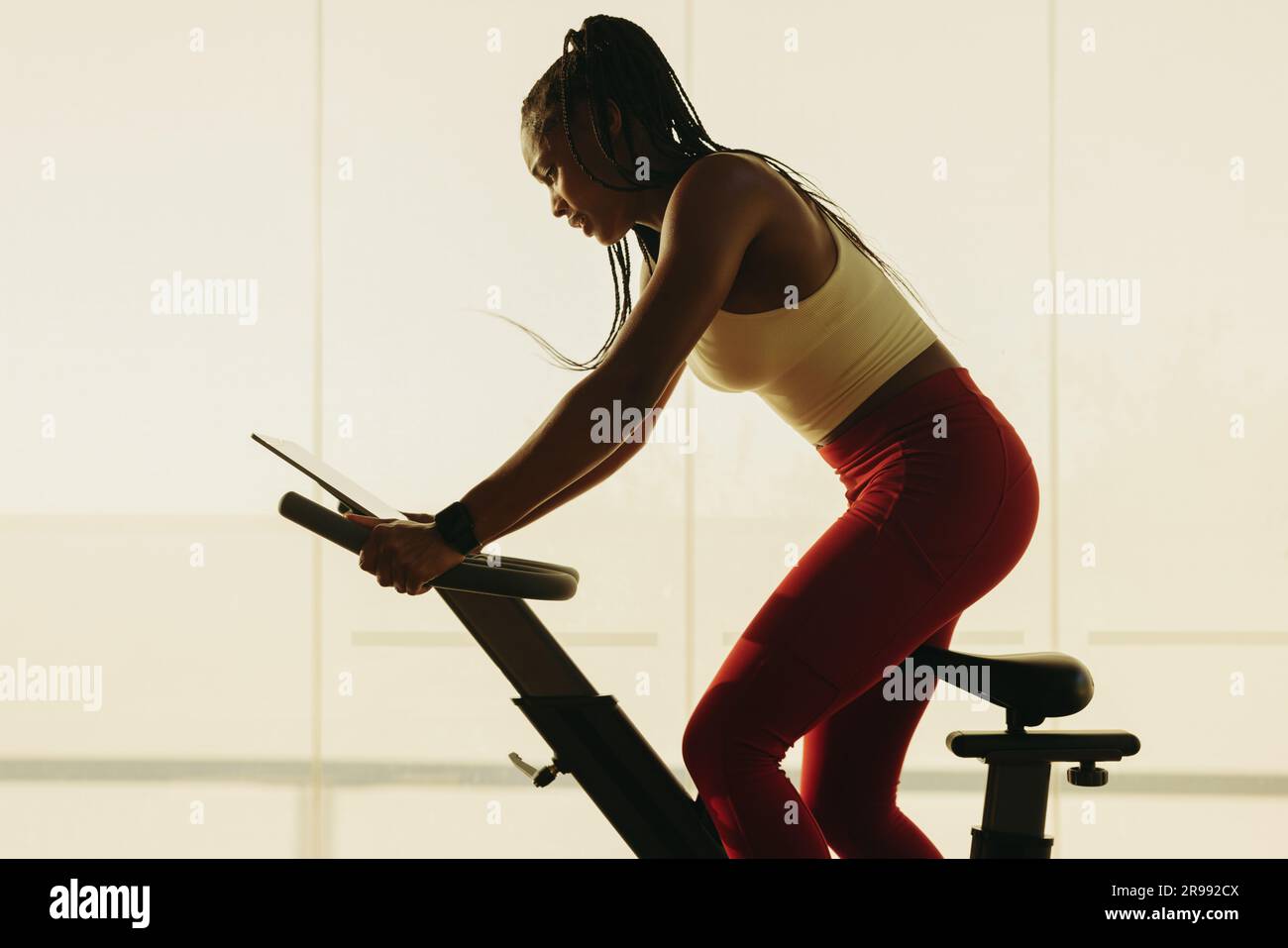 Fit, sportlich gekleidet, Pedale auf einem Heimtrainer in ihrem Fitness-Workout. Junge Frau, die ihr Engagement für die Erhaltung zeigt Stockfoto