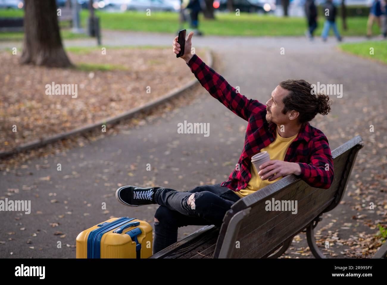 Ein Tourist mit einem fahrbaren Koffer, der Selfie in einem Park macht Stockfoto