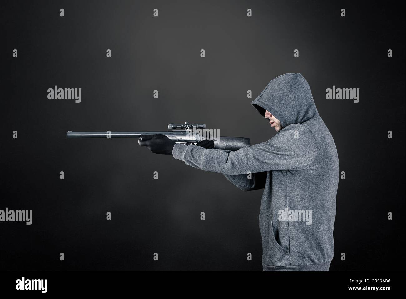 Ein Mann mit Kapuze und Gewehr auf dunklem nebligen Hintergrund Stockfoto