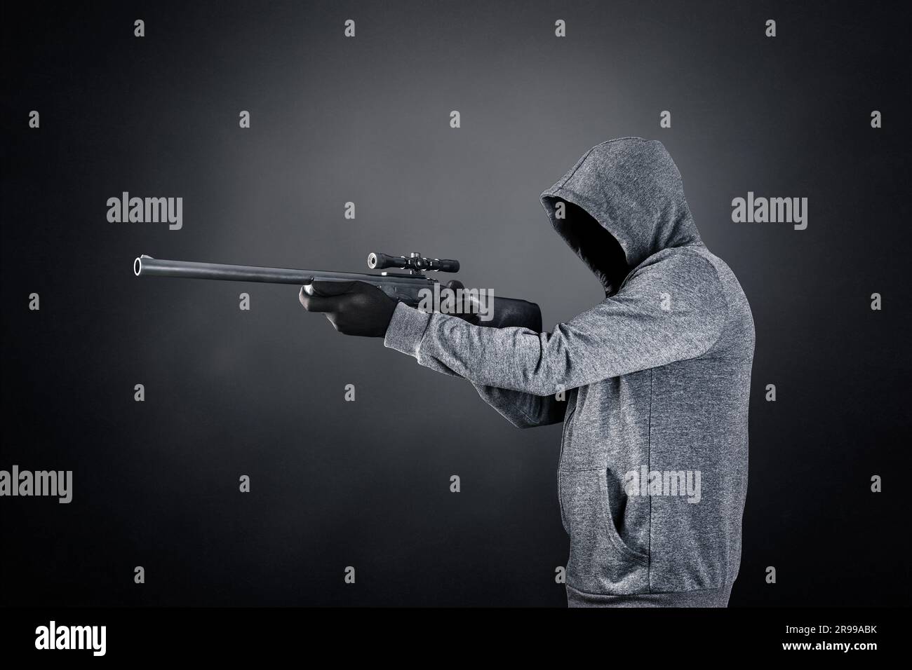 Ein Mann mit Kapuze und Gewehr auf dunklem nebligen Hintergrund Stockfoto