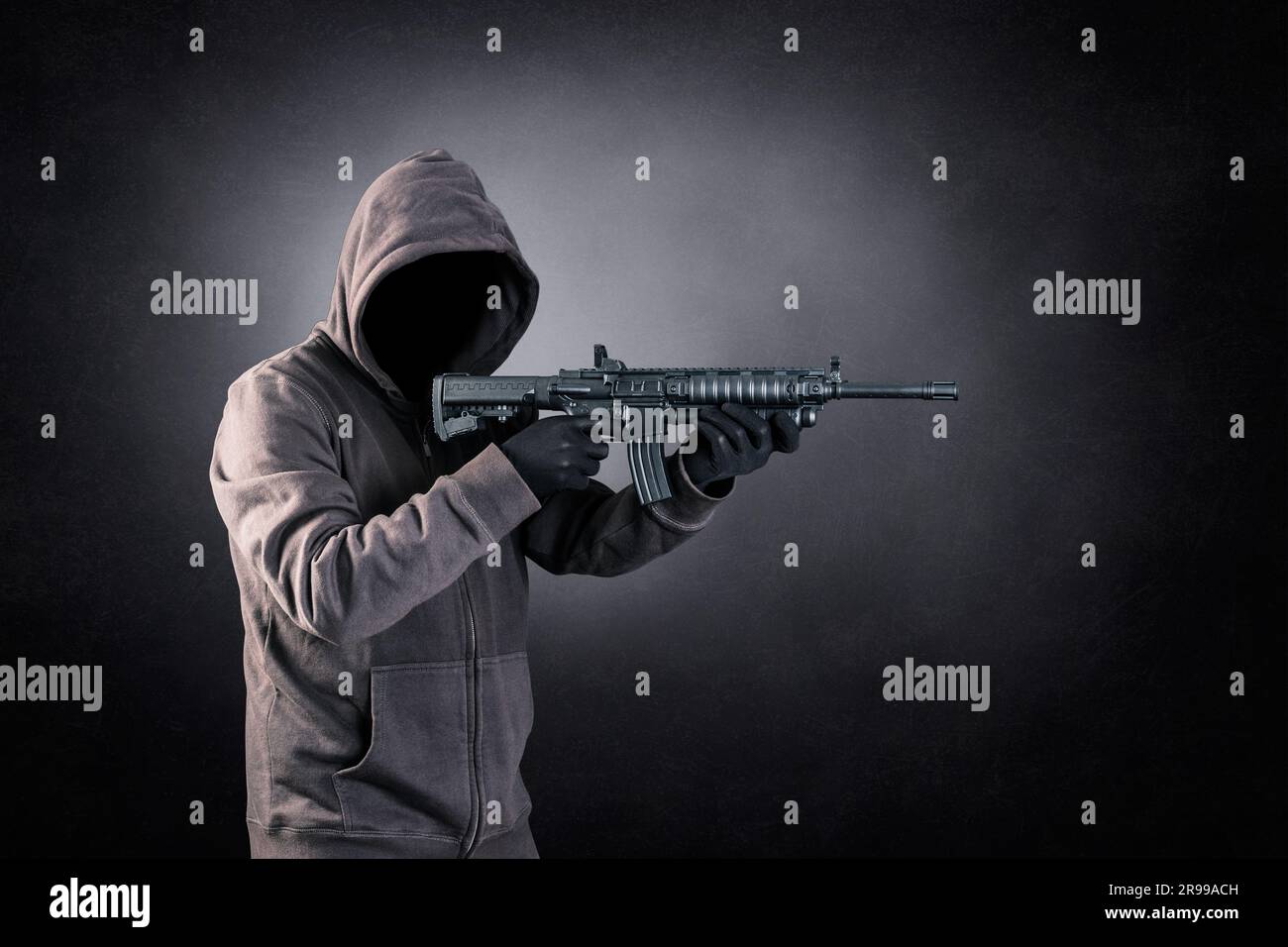 Ein Mann mit Kapuze und Sturmgewehr vor dunklem, nebligen Hintergrund Stockfoto