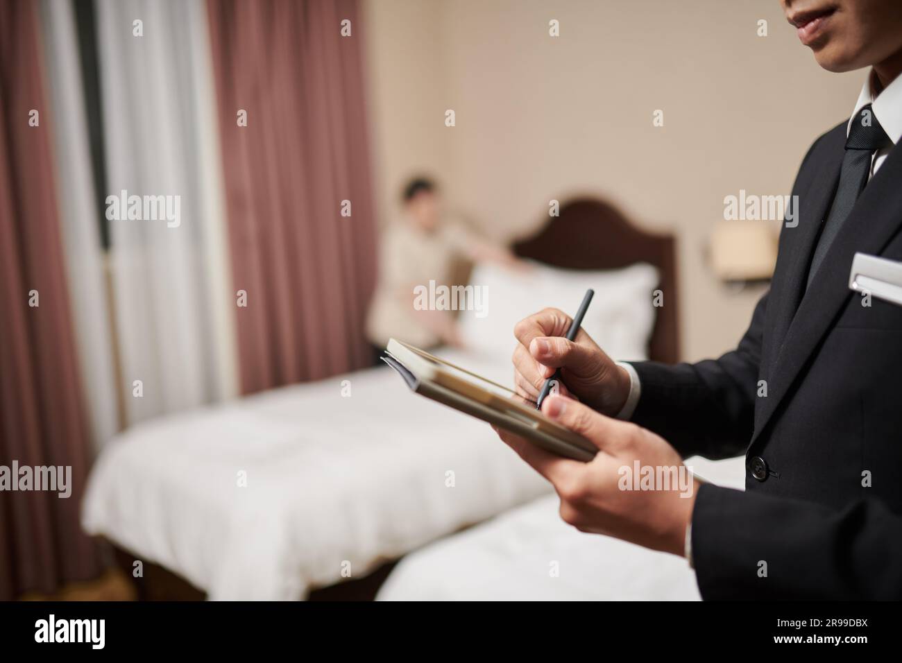 Der Hotelmanager überprüfte die Zimmerliste, als das Zimmermädchen die Bettwäsche wechselte Stockfoto