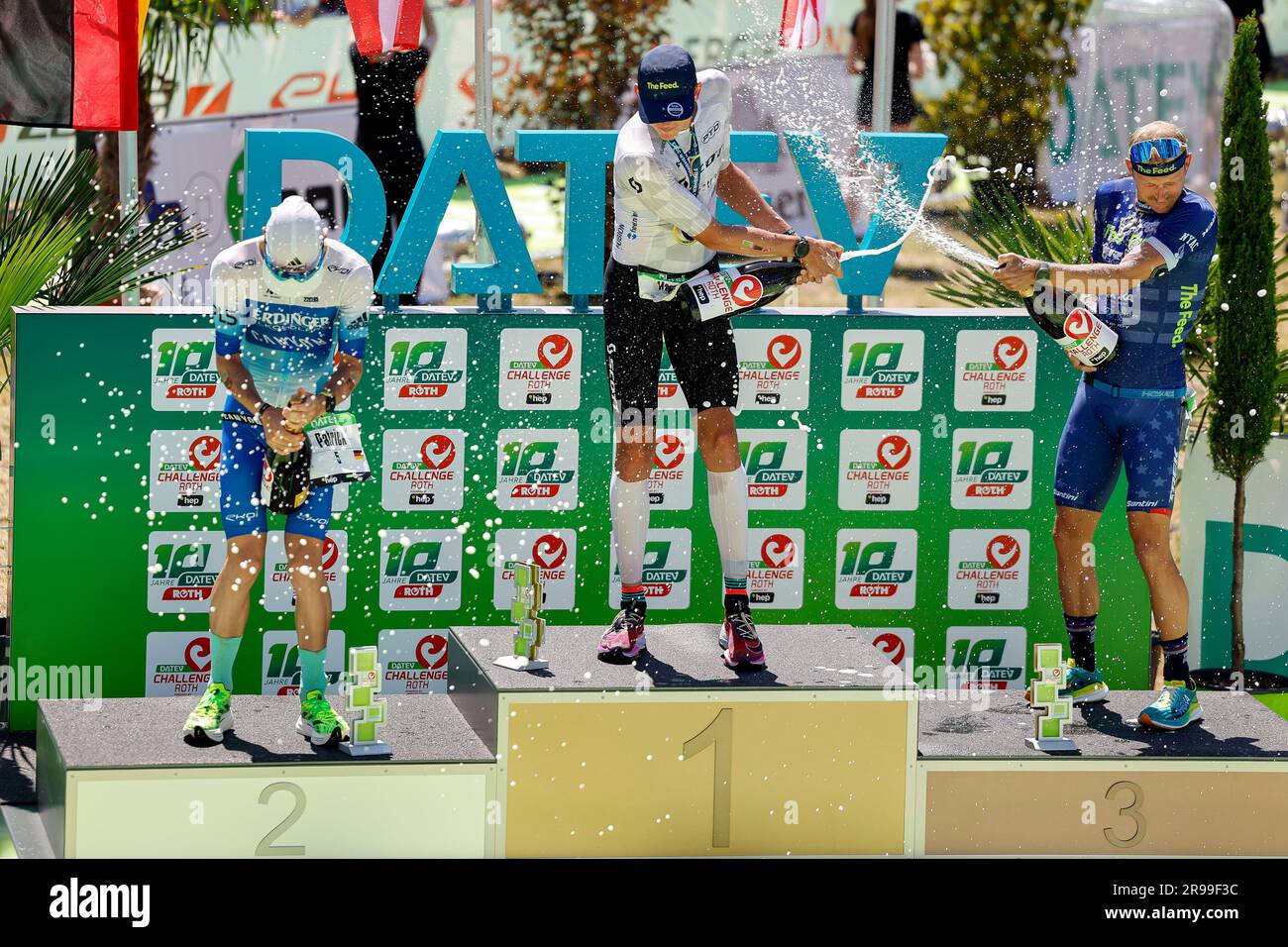 Roth, Deutschland. 25. Juni 2023. Triathlon: Challenge Roth, 3,86 km Schwimmen, 180,2 km Fahrrad, 42,2 km Laufen. Zweitplatzierter Patrick lange (l-r), Gewinner Magnus Ditlev und dritter Platz Ben Kanute der diesjährigen Triathlon Challenge Roth auf dem Podium mit Champagnerdusche. Kredit: Daniel Löb/dpa/Alamy Live News Stockfoto