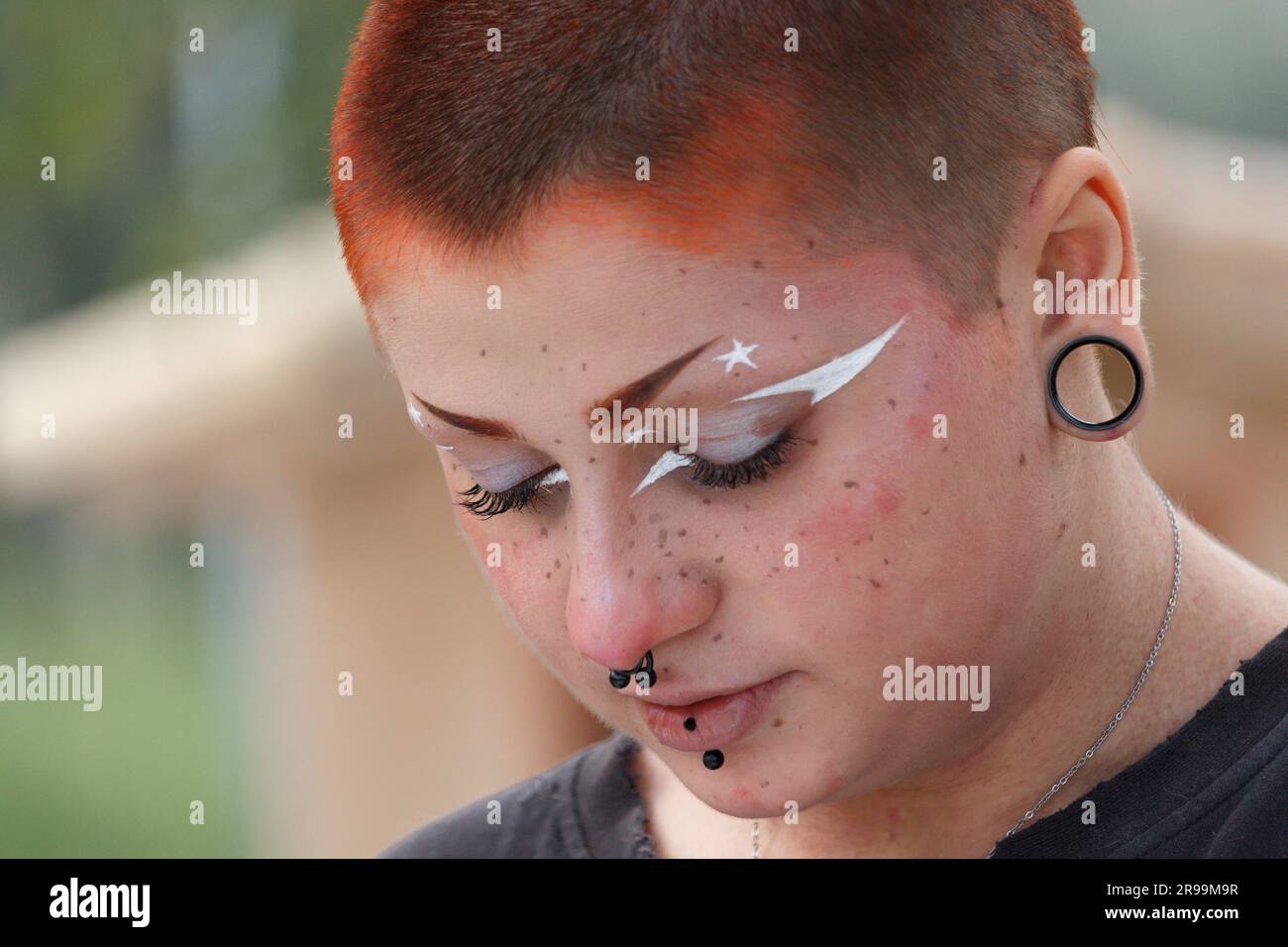 Eine Frau mit Piercings, die nach unten blickt, mit einem durchdachten Gesichtsausdruck Stockfoto