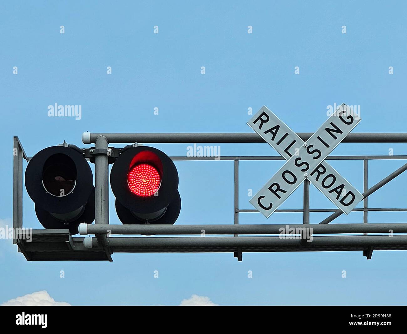 Bahnübergangsschild mit blinkender roter Ampel am blauen Himmel Stockfoto