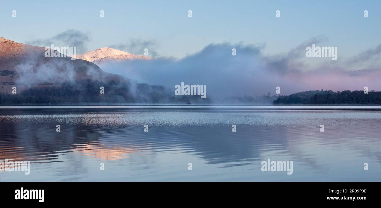 Blick auf den nebeligen See mit reflektierten schneebedeckten Bergen Stockfoto