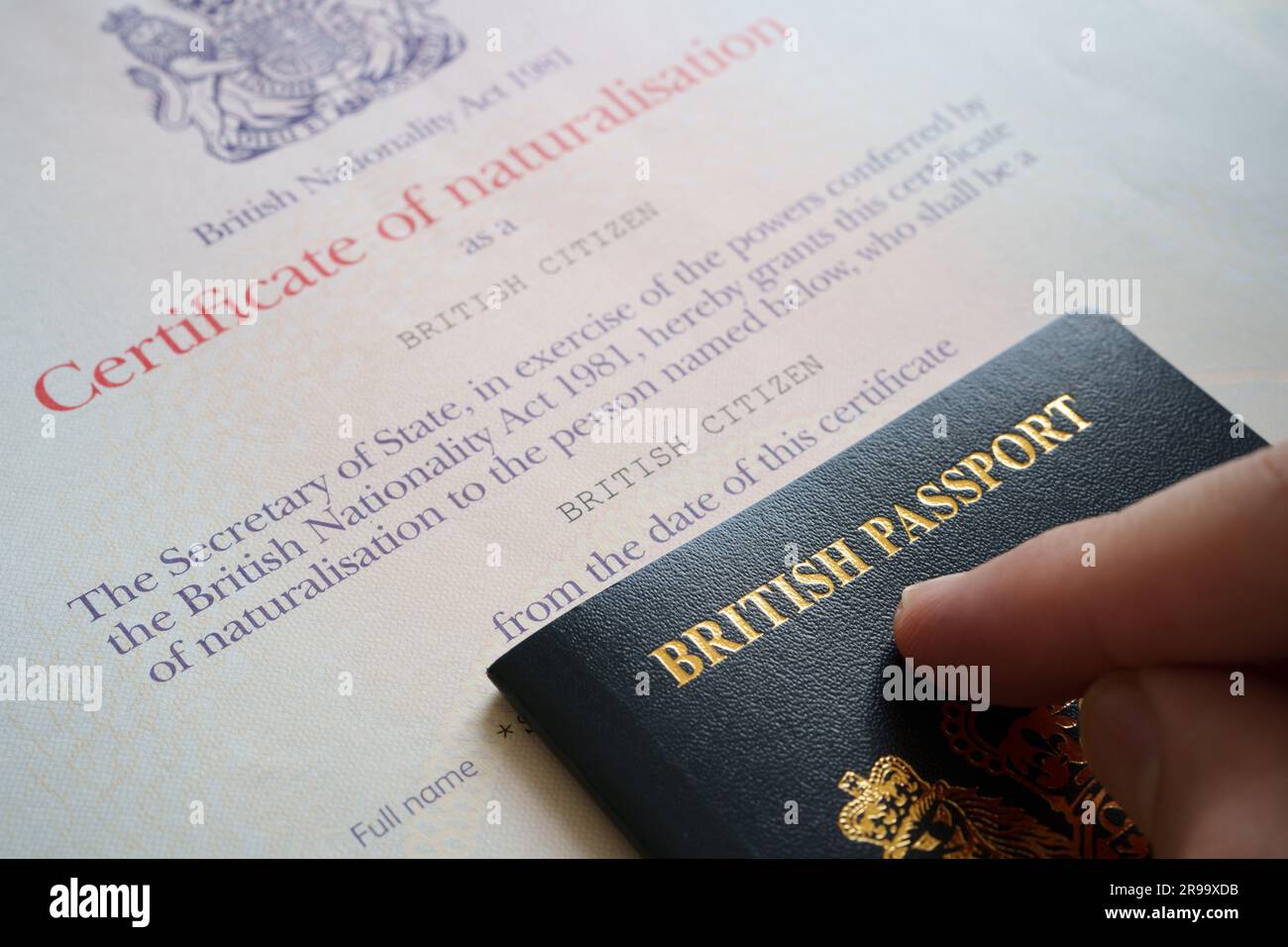 Hand zeigt auf britischen Pass und Einbürgerungszertifikat als britischer Staatsbürger. Authentische Dokumente. Stafford, Großbritannien, 25. Juni 2023 Stockfoto