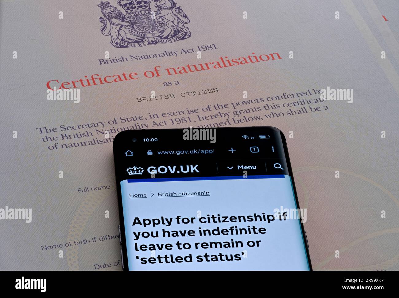 Smartphone mit Online-Bewerbungsseite für die Staatsbürgerschaft, die über dem Einbürgerungszertifikat als britischer Staatsbürger platziert wird. Stafford, Großbritannien, Jun Stockfoto