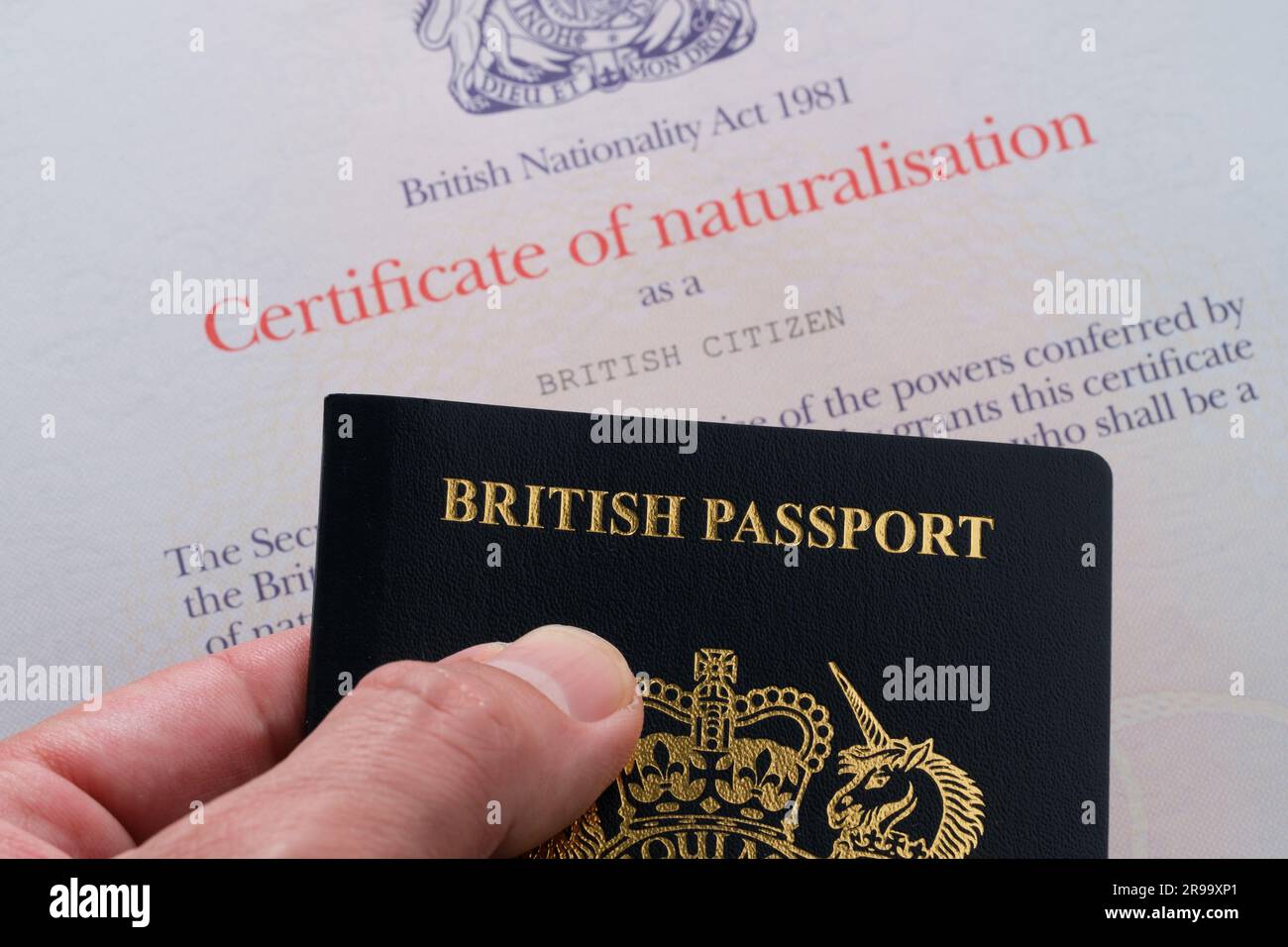 Hand mit britischem Reisepass neben dem Einbürgerungszertifikat als britischer Staatsbürger. Stafford, Großbritannien, 25. Juni 2023 Stockfoto