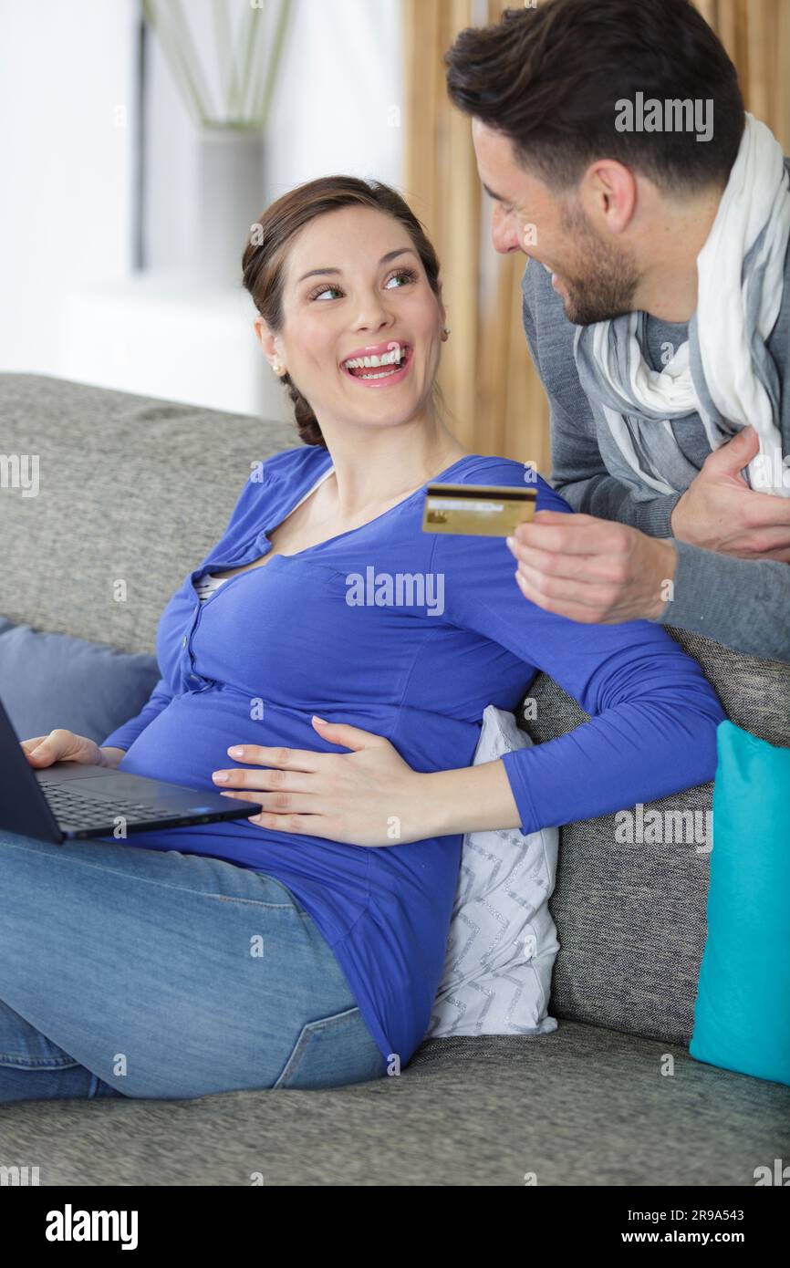 Glückliches schwangeres Paar mit Kreditkarte, das auf dem Sofa saß Stockfoto
