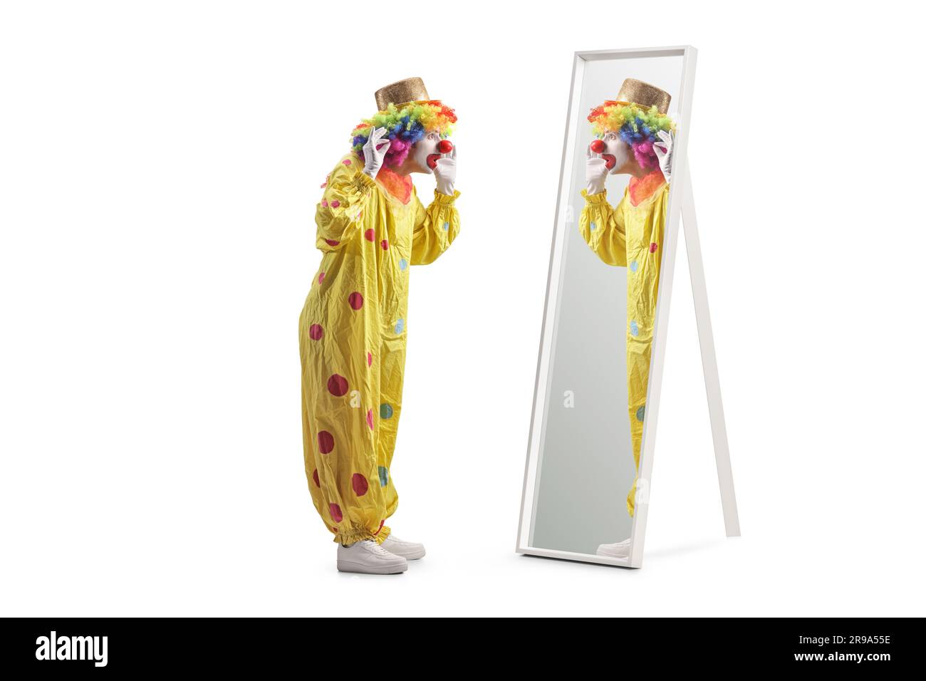 Ein Clown in einem gelben Kostüm, der vor einem Spiegel steht, isoliert auf weißem Hintergrund Stockfoto
