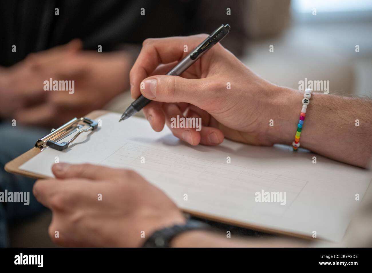 Ein erwachsener Mann hält ein Klemmbrett, während er in einer Therapiesitzung sitzt Stockfoto