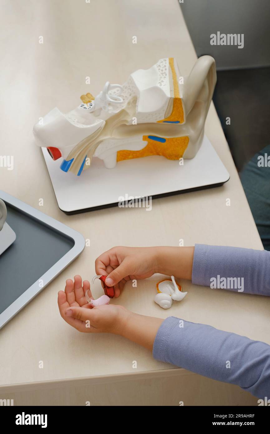 Kindgerechte Hörgeräte in der Medizinischen Klinik, Ohrmodell im Hintergrund. Ein Kind mit Hörverlust-Tring-Abhörgerät. Nahaufnahme der Hände. Draufsicht Stockfoto