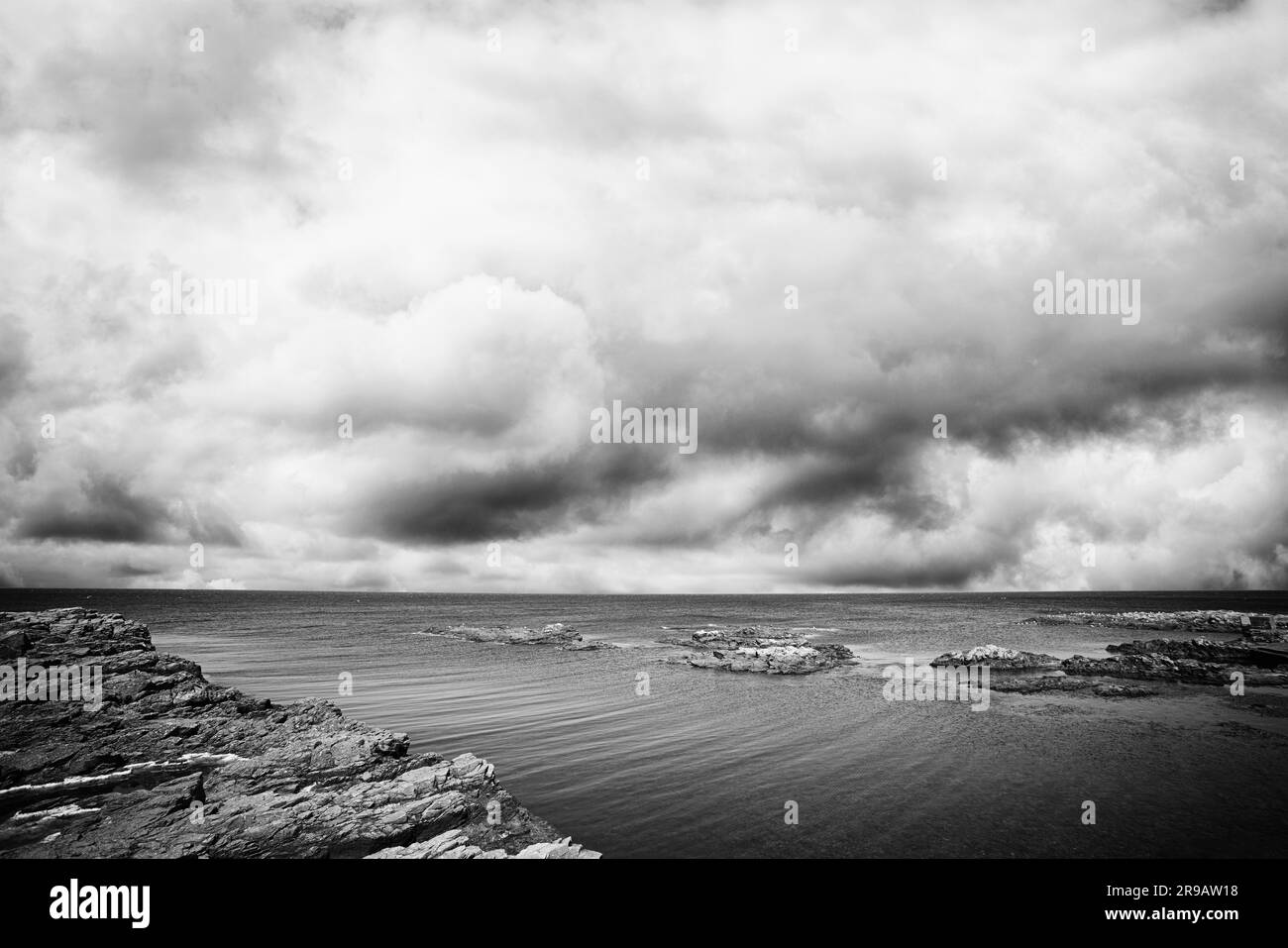 Felsen am Ufer des Meeres mit dramatischen dunkle Wolken kommen in Schwarzweiß Ton Stockfoto