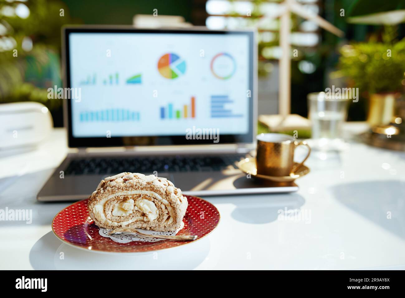 Psychische Gesundheit am Arbeitsplatz. Nahaufnahme auf einem Tisch in einem modernen Büro mit einem Stück Kuchen, einer Tasse Kaffee und einem Laptop. Stockfoto