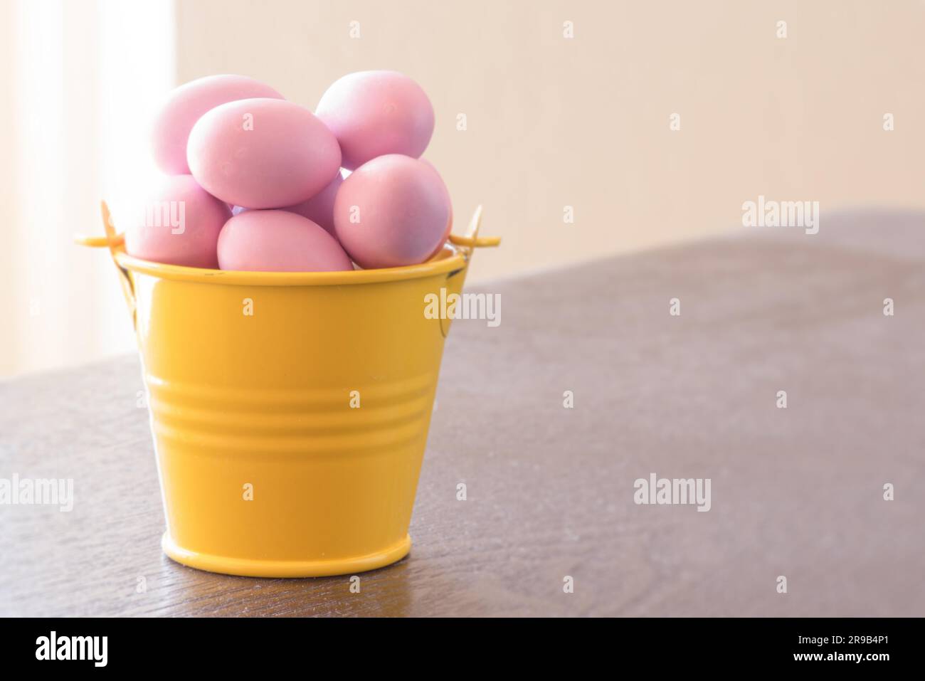 Gelber Eimer mit violetten Ostern Eiern auf einem Tisch Stockfoto