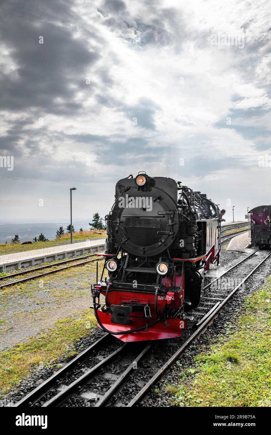 Schwarze Lokomotive mit roter Farbe, die auf einer Eisenbahnstrecke unter einem bewölkten Himmel fährt Stockfoto