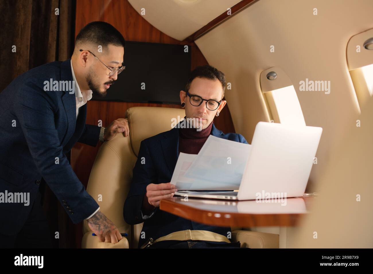 Elegantes Geschäftsmannspaar, das in einem Privatflugzeug sitzt und während des Fluges über die Arbeit spricht, während es sich Laptop, Travel und Airline ansieht Stockfoto