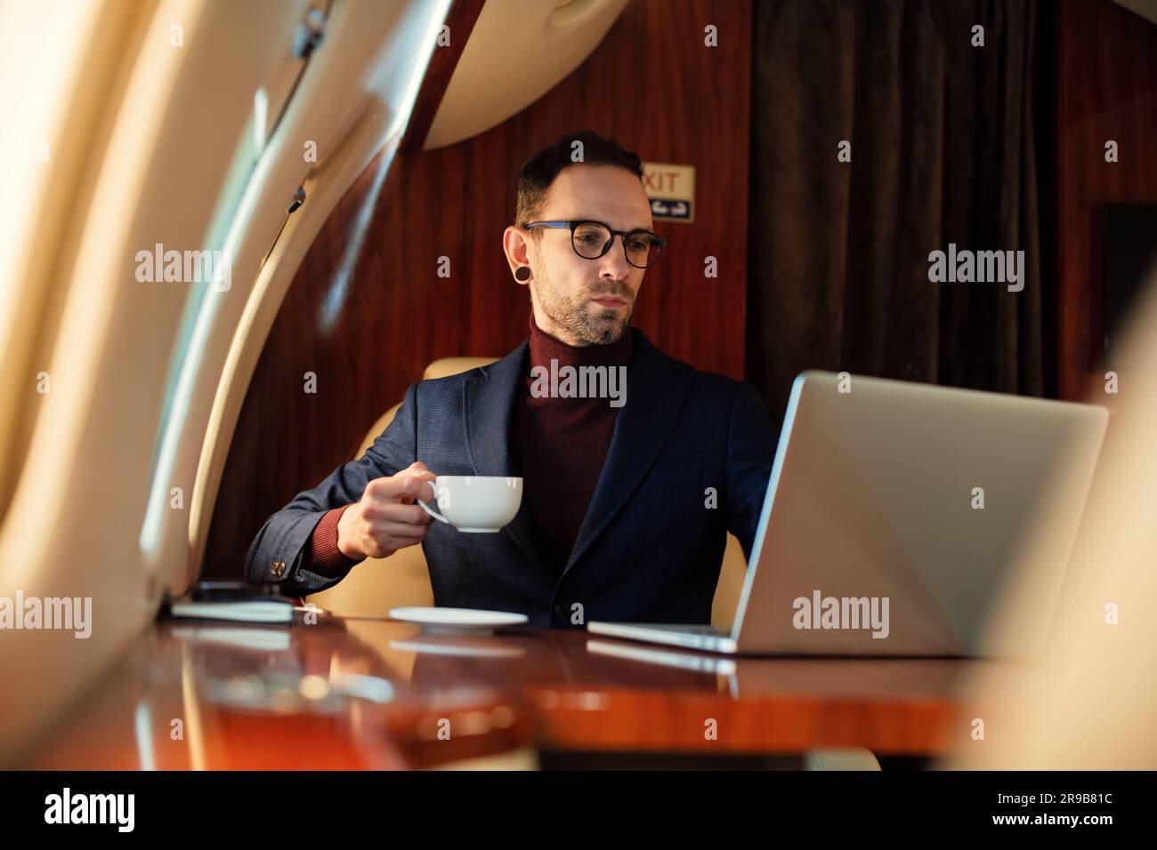 Junger Geschäftsmann mit Brille trinkt Kaffee in der ersten Klasse eines Privatflugzeuges Stockfoto