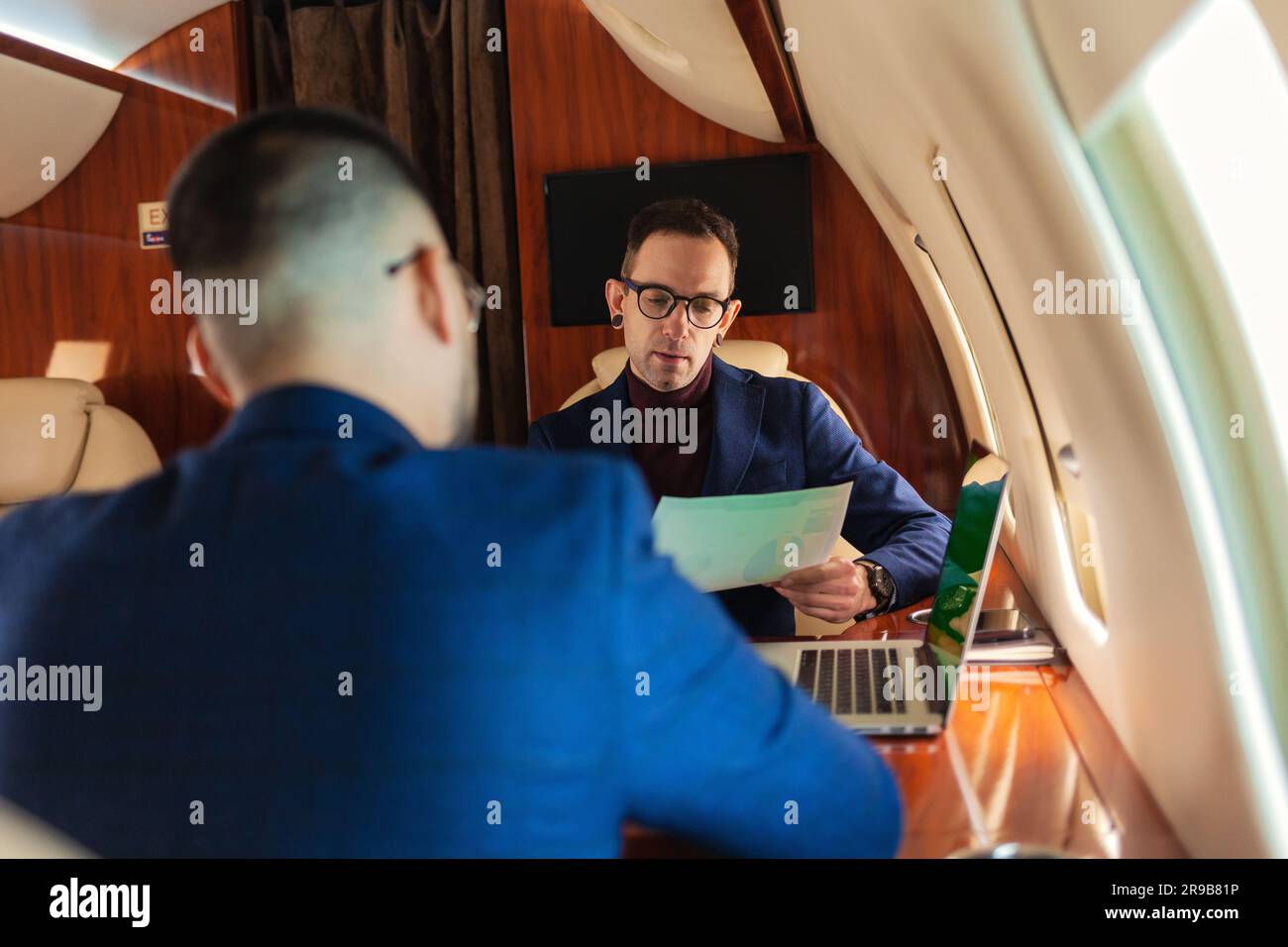 Zwei Geschäftsleute sitzen in einem privaten Jet-Flugzeug und reden über die Arbeit, die Hand schüttelt, während im Flug Geschäftskonzept der Travel Airline Stockfoto