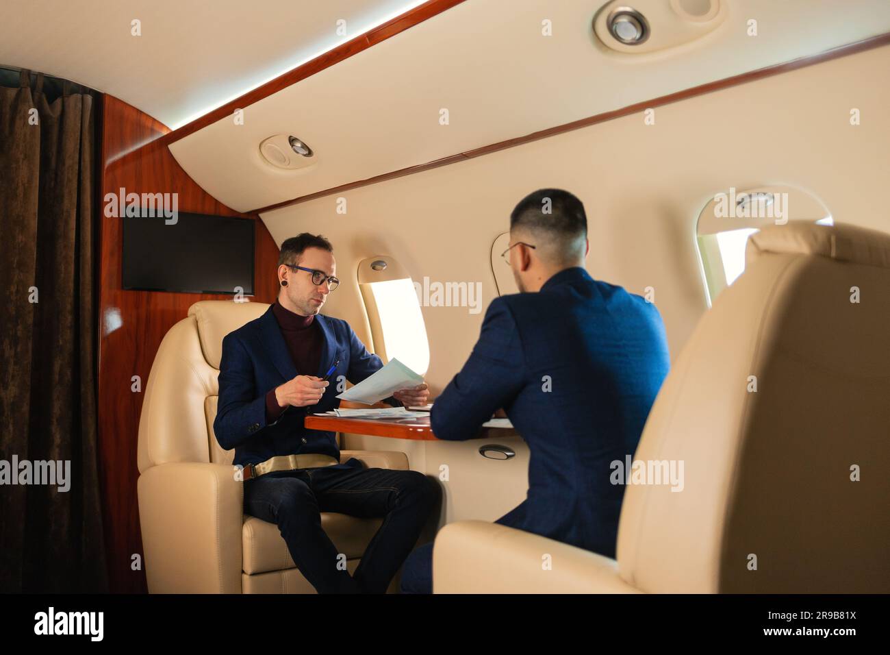 Zwei Geschäftsleute sitzen in einem privaten Jet-Flugzeug und reden über die Arbeit, die Hand schüttelt, während im Flug Geschäftskonzept der Travel Airline Stockfoto