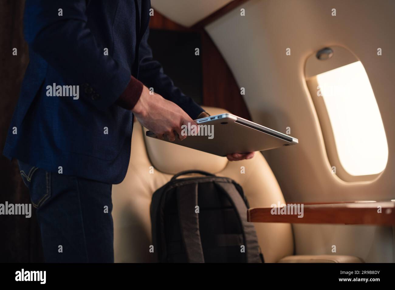 Ein nicht erkennbarer Geschäftsmann zieht einen modernen Windows-Laptop heraus und legt ihn auf den Tisch, um in einem erstklassigen Privatflugzeug zu arbeiten Stockfoto