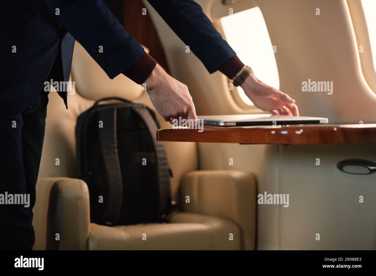 Ein unerkannter Geschäftsmann aus der Nähe zieht einen modernen Windows-Laptop heraus und stellt ihn auf den Tisch, um in einem erstklassigen Privatflugzeug zu arbeiten Stockfoto