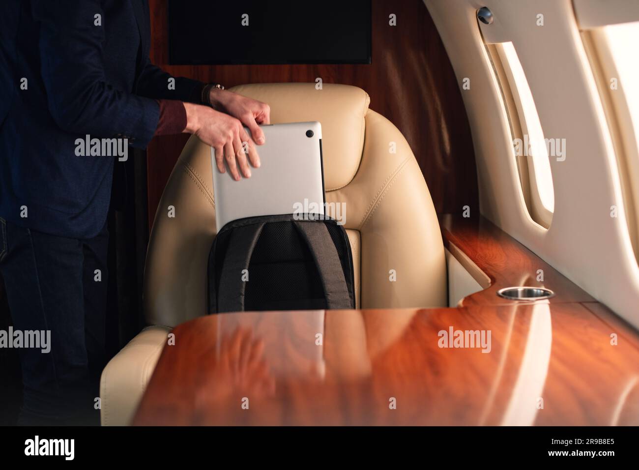 Ein eleganter Geschäftsmann aus der Nähe zieht einen modernen Laptop heraus und stellt ihn auf den Tisch, um von dort aus in einem erstklassigen Privatflugzeug zu arbeiten Stockfoto