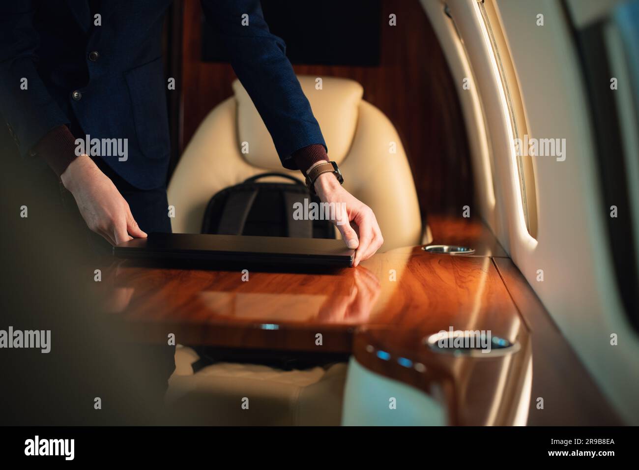 Ein unerkannter Geschäftsmann aus der Nähe zieht einen modernen Windows-Laptop heraus und stellt ihn auf den Tisch, um in einem erstklassigen Privatflugzeug zu arbeiten Stockfoto