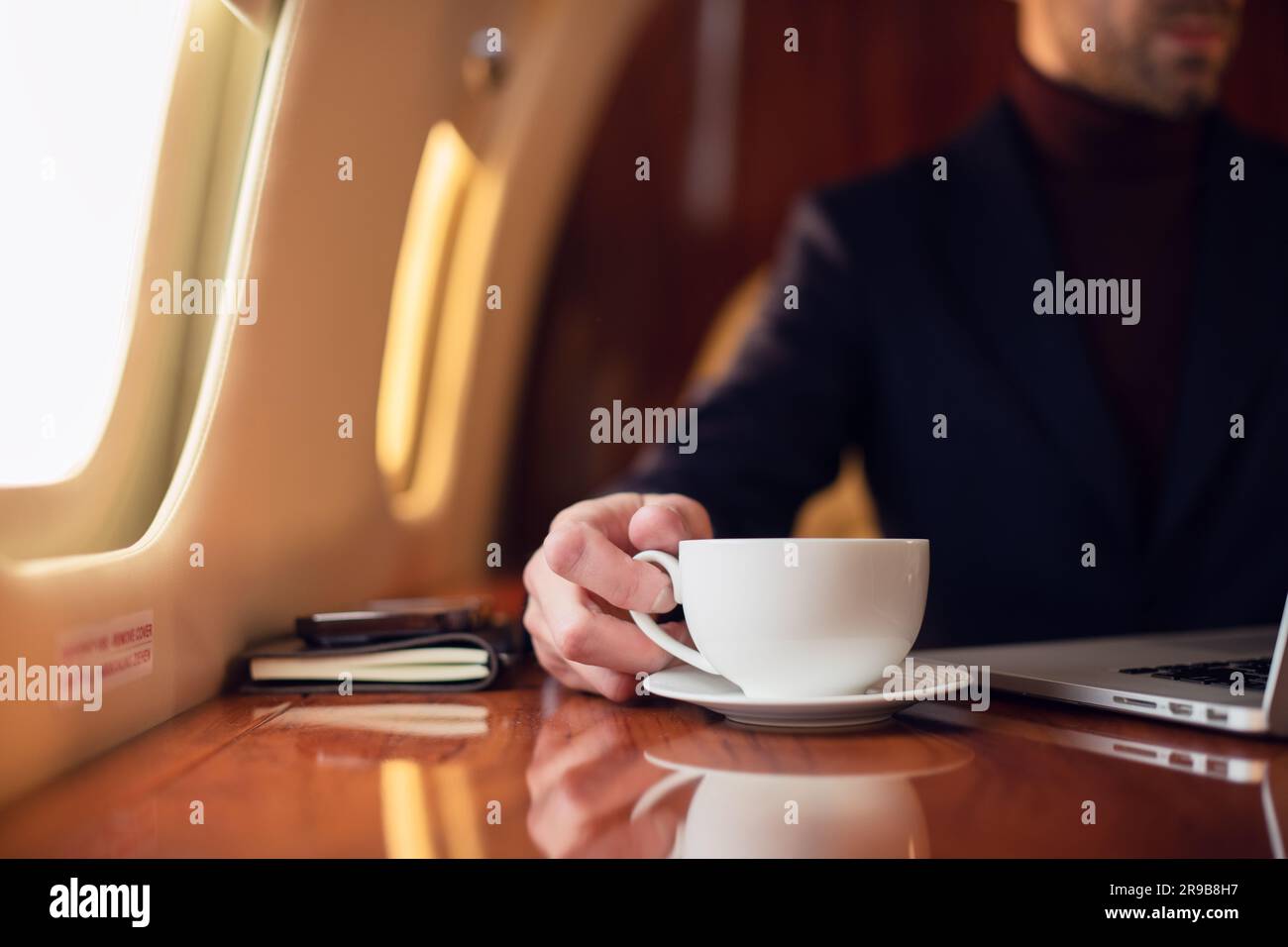 Nahaufnahme des Geschäftsmannes, der im privaten Flugzeug Jet nach einer Tasse Kaffee streckt, eleganter junger Geschäftsmann mit Brille, der im Privatjet sitzt Stockfoto