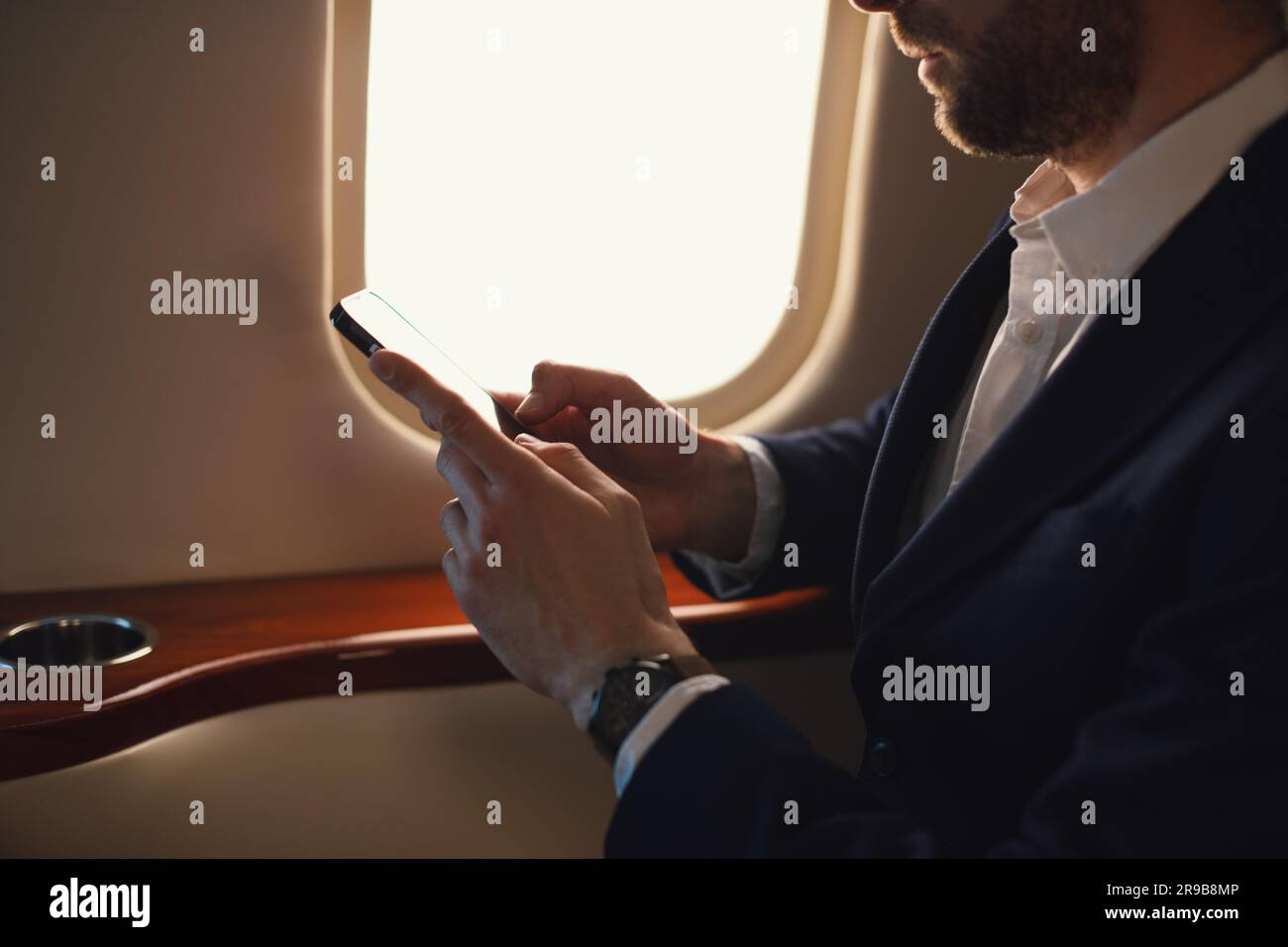 Eleganter CEO junger, selbstbewusster Geschäftsmann mit Brille Mann sitzt in einem erstklassigen Privatjet und arbeitet mit einem modernen Smartphone aus nächster Nähe Stockfoto