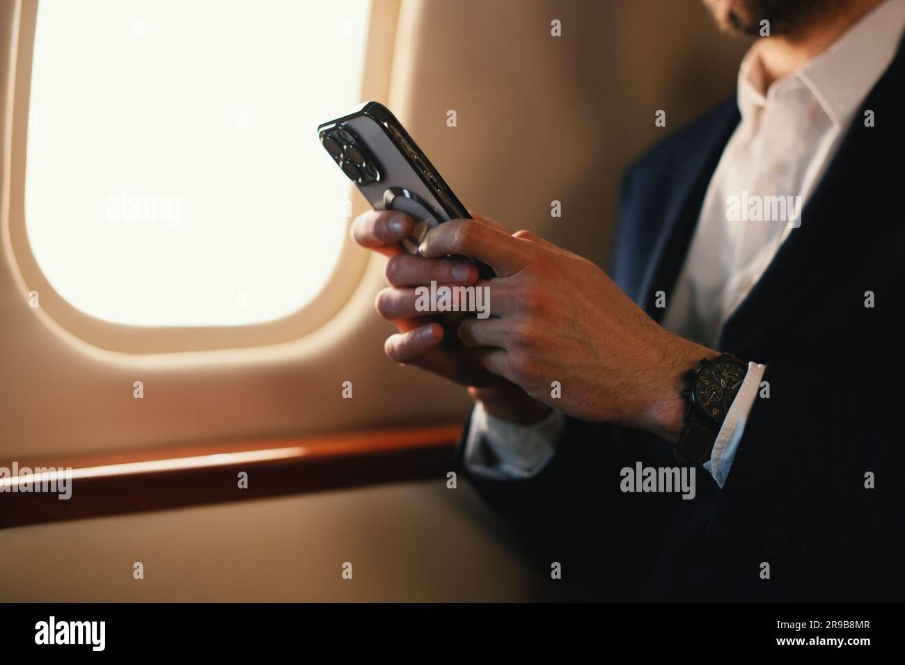 Eleganter CEO junger, selbstbewusster Geschäftsmann mit Brille Mann sitzt in einem erstklassigen Privatjet und arbeitet mit einem modernen Smartphone aus nächster Nähe Stockfoto