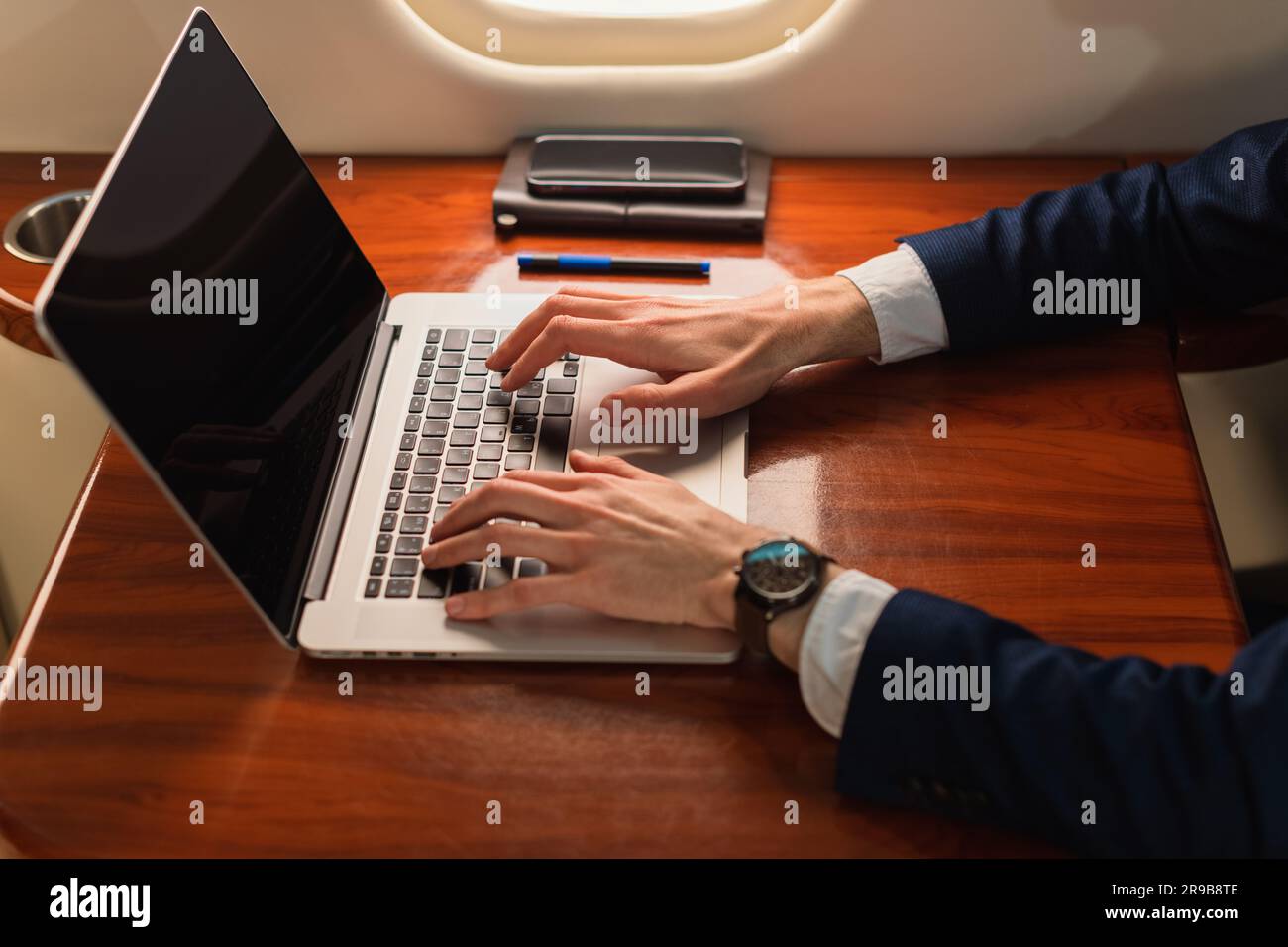 Aus der Nähe unwiedererkennbarer eleganter Geschäftsführer, der an einem modernen Laptop arbeitet, in einem Privatflugzeug der ersten Klasse, Side View Stockfoto