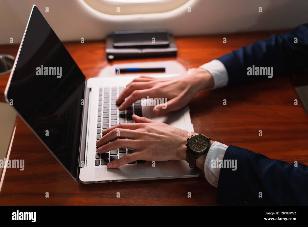 Aus der Nähe unwiedererkennbarer eleganter Geschäftsführer, der an einem modernen Laptop arbeitet, in einem Privatflugzeug der ersten Klasse, Side View Stockfoto