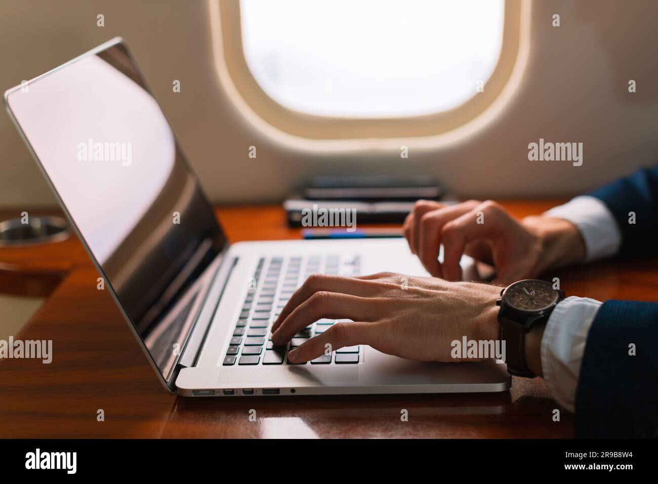 Aus der Nähe unwiedererkennbarer eleganter Geschäftsführer, der an einem modernen Laptop arbeitet, in einem Privatflugzeug der ersten Klasse, Side View Stockfoto