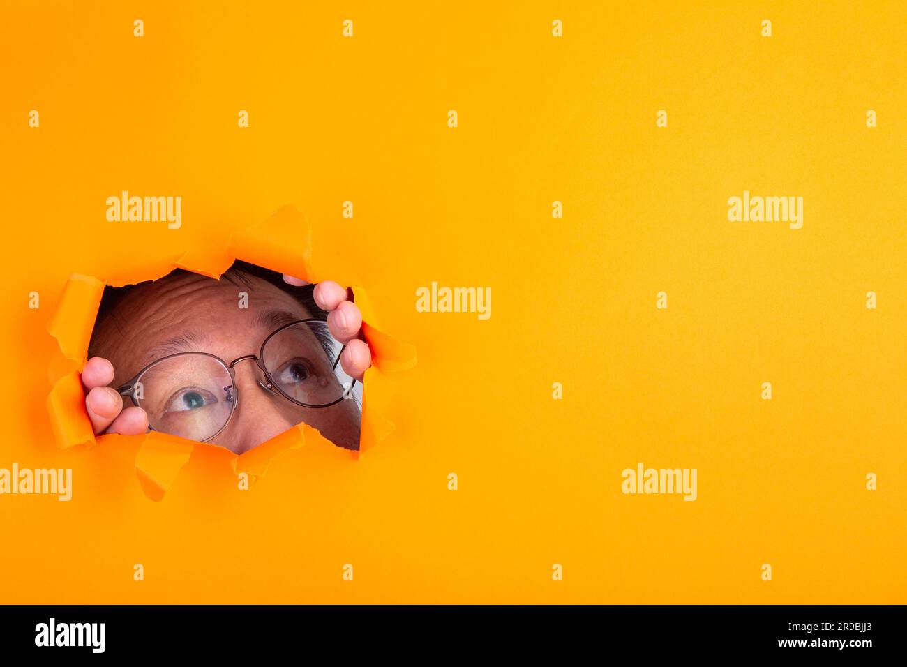 Ein Mann mit Brille, der durch ein Loch in orangefarbenem Papier ragt Stockfoto