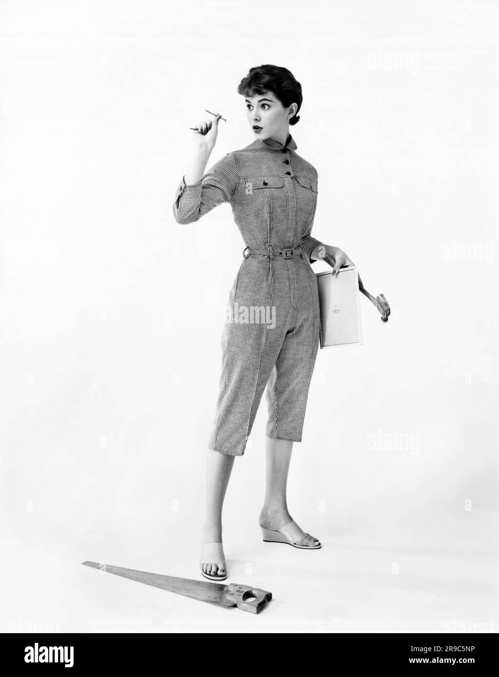 USA: ca. 1957 Eine junge Frau in modischen BaumwollOveralls bereitet sich auf einige Reparaturen vor. Stockfoto