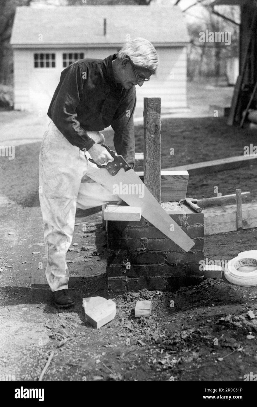 New York, New York: 1922 Schauspieler und Dramatiker Frank Bacon sägt ein Stück Holz in seinem Haus in Bayside in Queens auf Long Island. Stockfoto