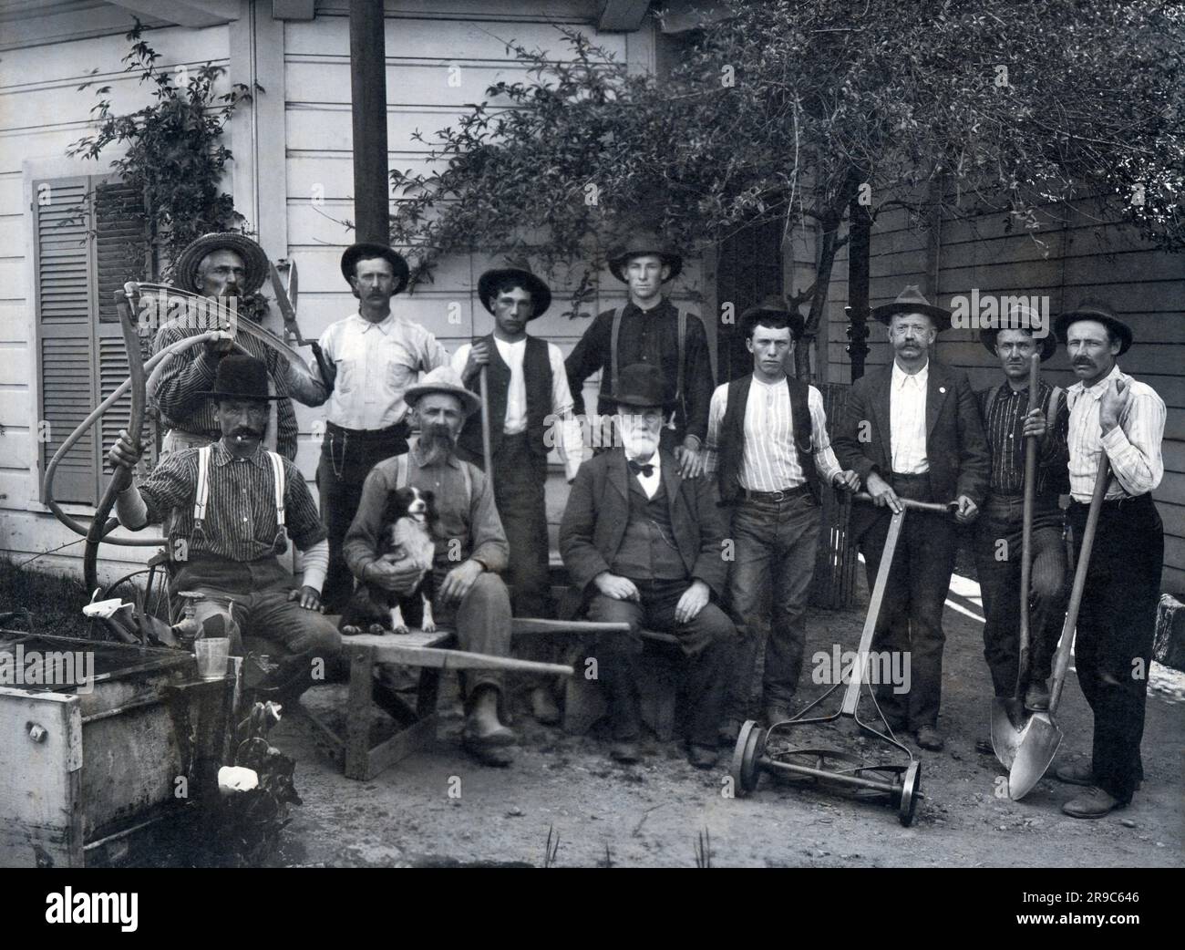 Vereinigte Staaten: c. 1900 ein älterer Mann mit Arbeitern und Landschaftsgestaltungsteam und deren Werkzeugen, einschließlich Schubkarre, Schaufeln, Schere, Rasenmäher und Sense. Stockfoto