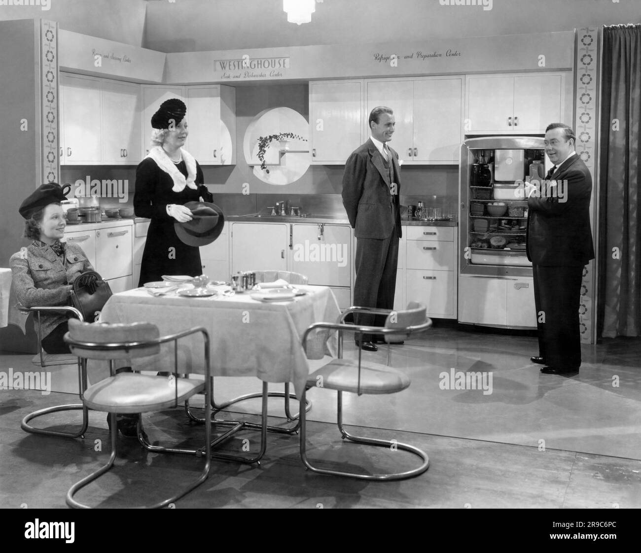 USA: 1939 Ein Verkäufer präsentiert potenziellen Käufern die Vorzüge von Westinghouse Kühlschränken in einem Westinghouse Modellküchen-Ausstellungsraum. Stockfoto