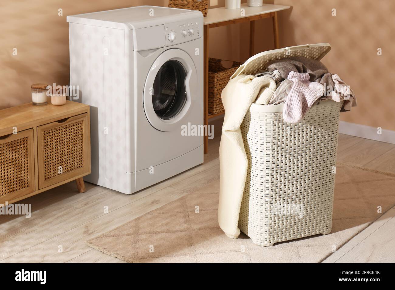 Wäschekorb überfüllt mit Wäsche in der Nähe der Waschmaschine im Badezimmer Stockfoto