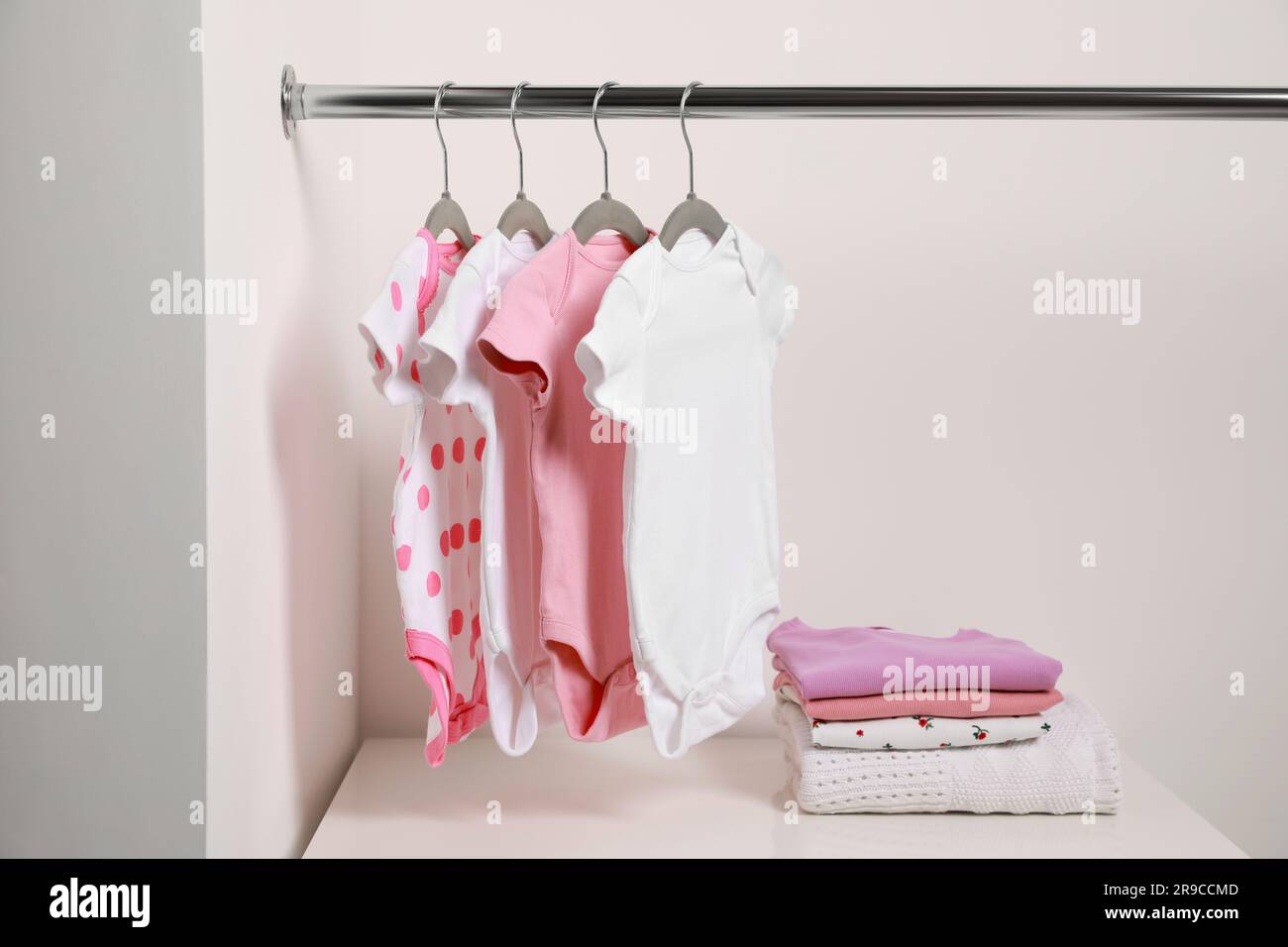 Kleiderbügel mit Babybekleidung und Kleiderstapel in der Nähe der weißen Wand Stockfoto