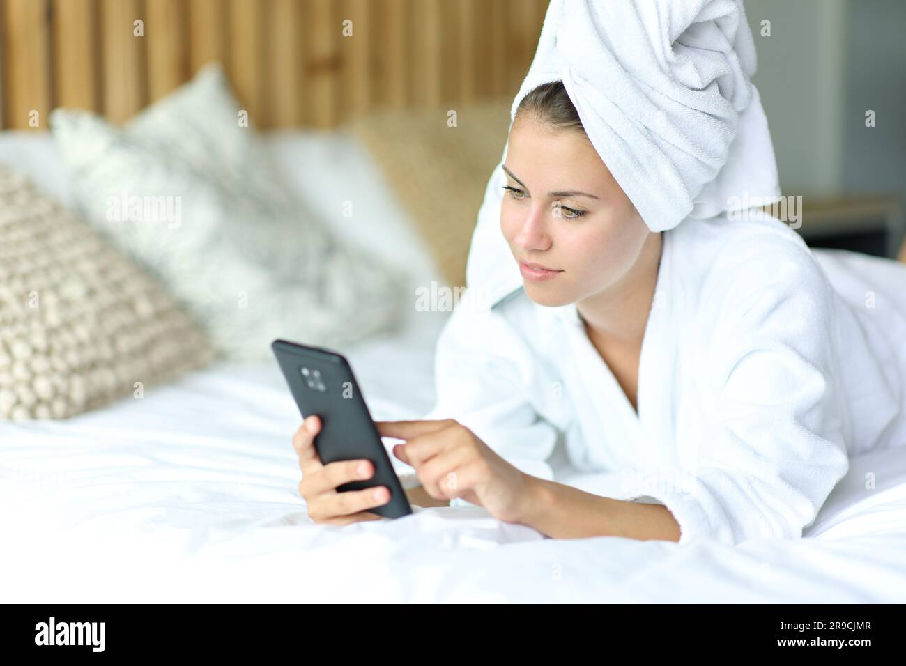 Zufriedene Frau, die nach dem Duschen das Telefon im Bett benutzte Stockfoto