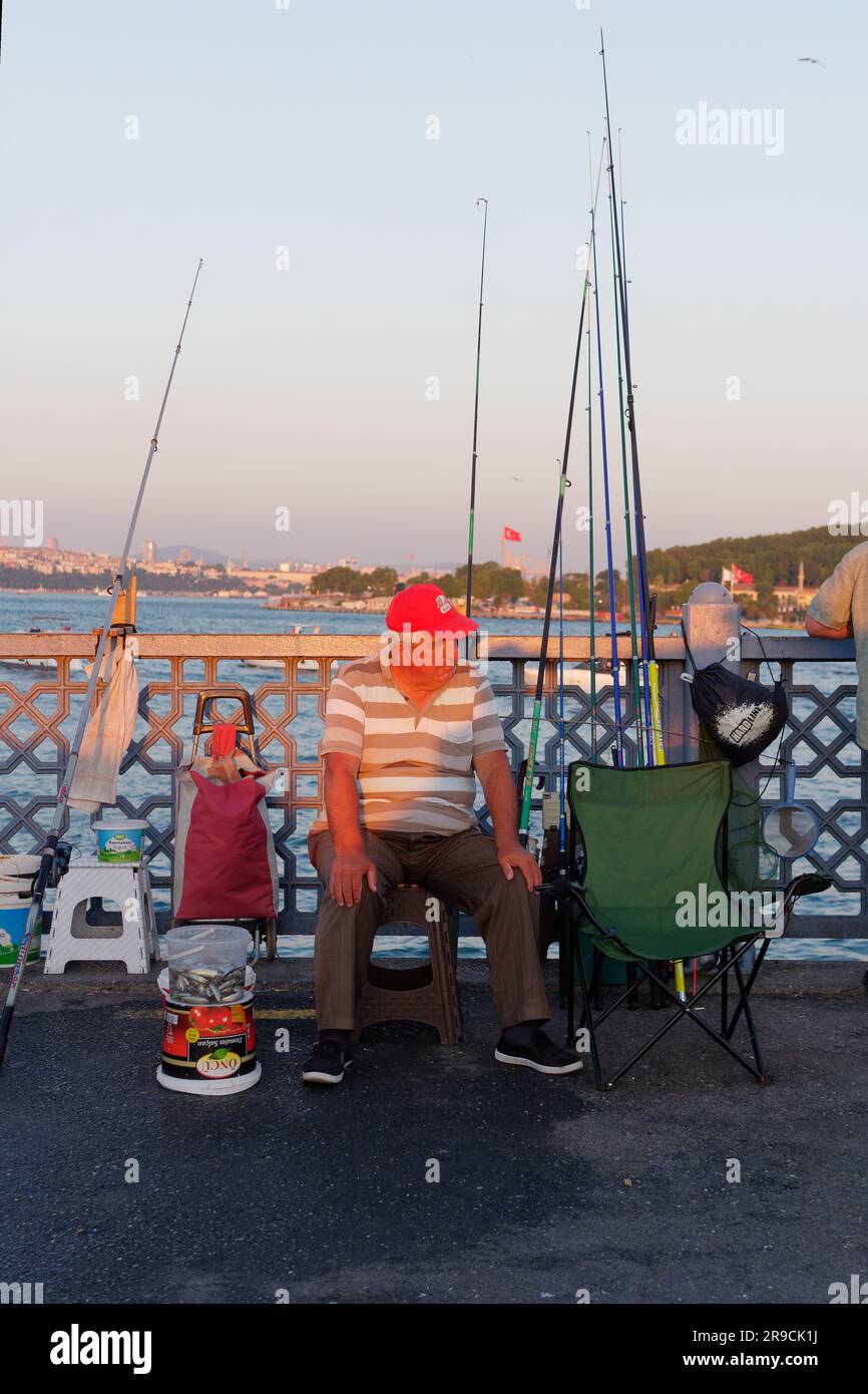 Ein einheimischer Fischer rastet an einem Sommerabend auf der Galta Bridge mit dem Goldenen Horn in Istanbul, Türkei, aus Stockfoto