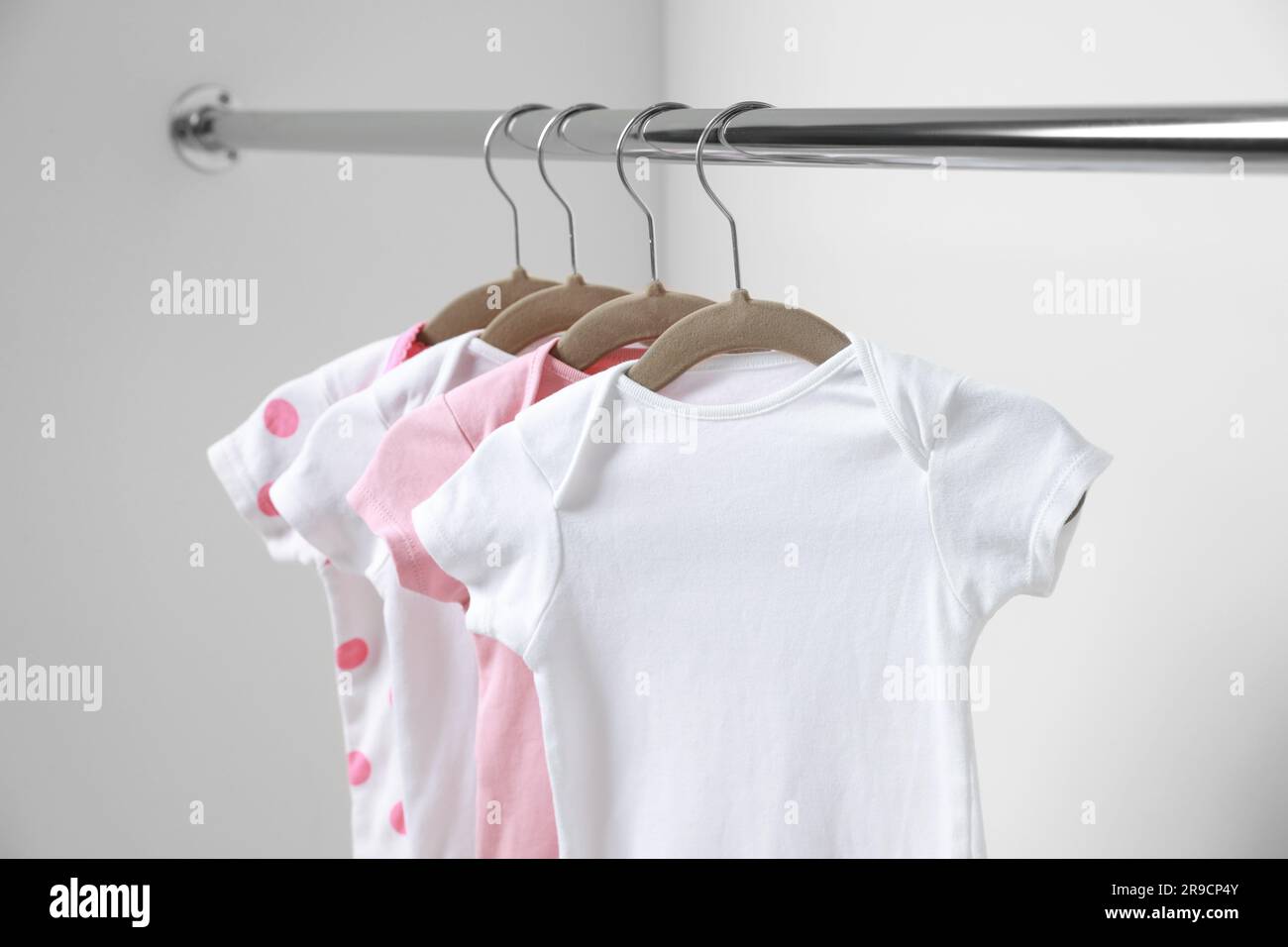 Babykleidung hängt an einem Regal nahe der weißen Wand, Nahaufnahme Stockfoto